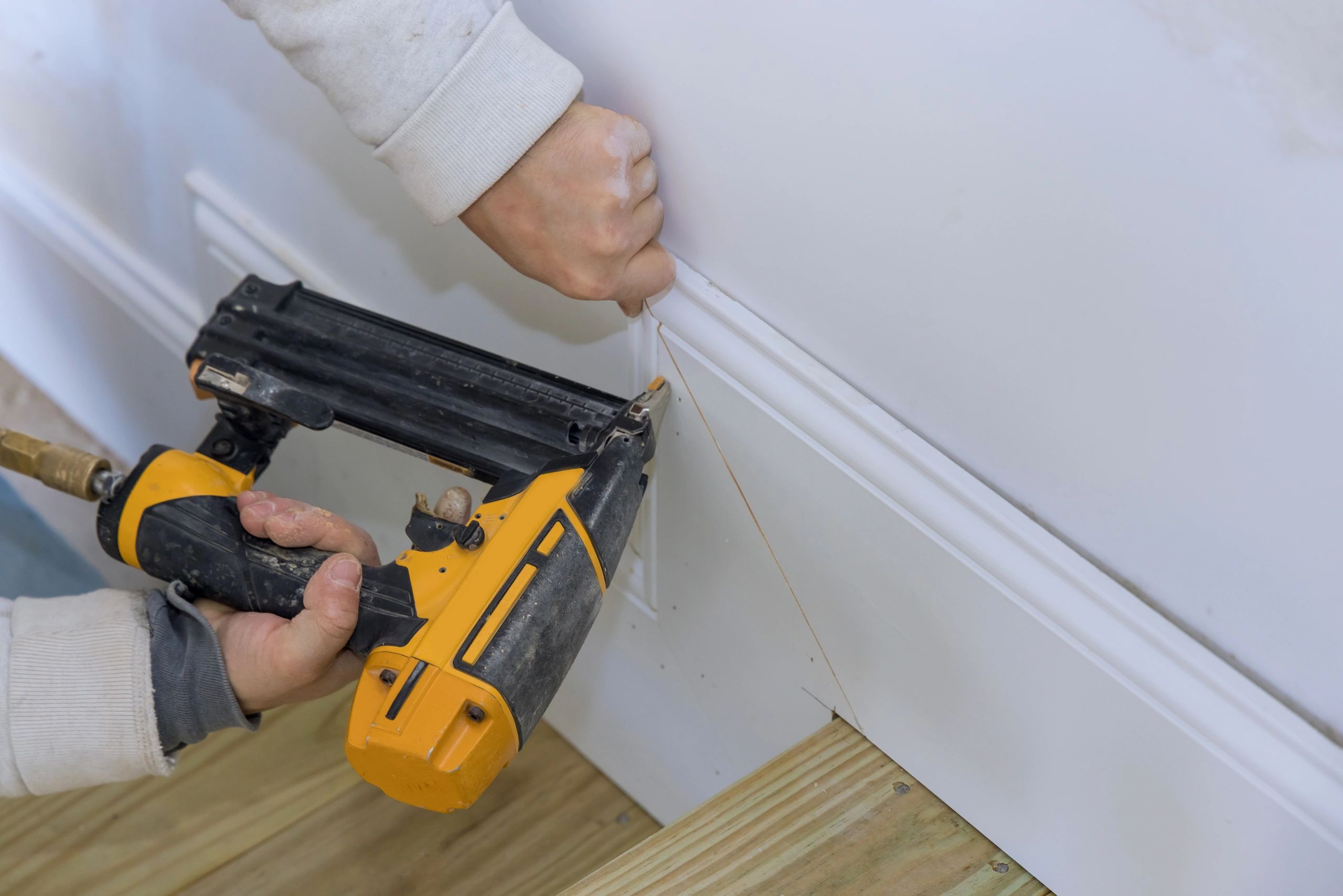 Carpenter installing baseboard trim with a nail gun